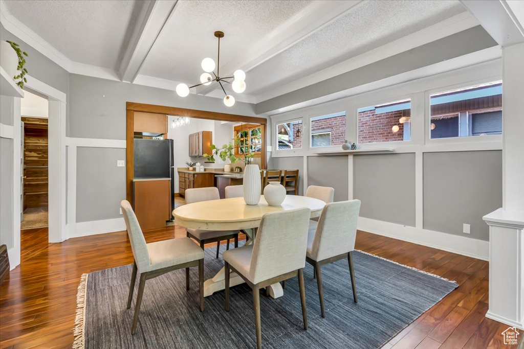 Dining space with a chandelier, a textured ceiling, wood finished floors, and beamed ceiling