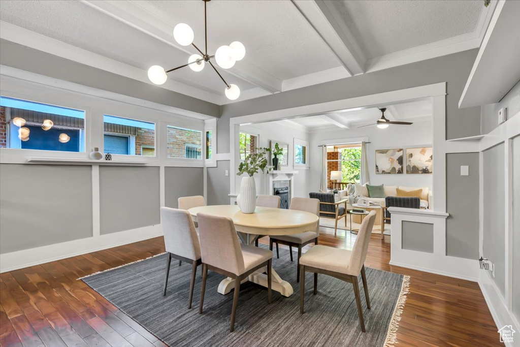 Dining area featuring wood-type flooring, beam ceiling, a fireplace, a chandelier, and ceiling fan