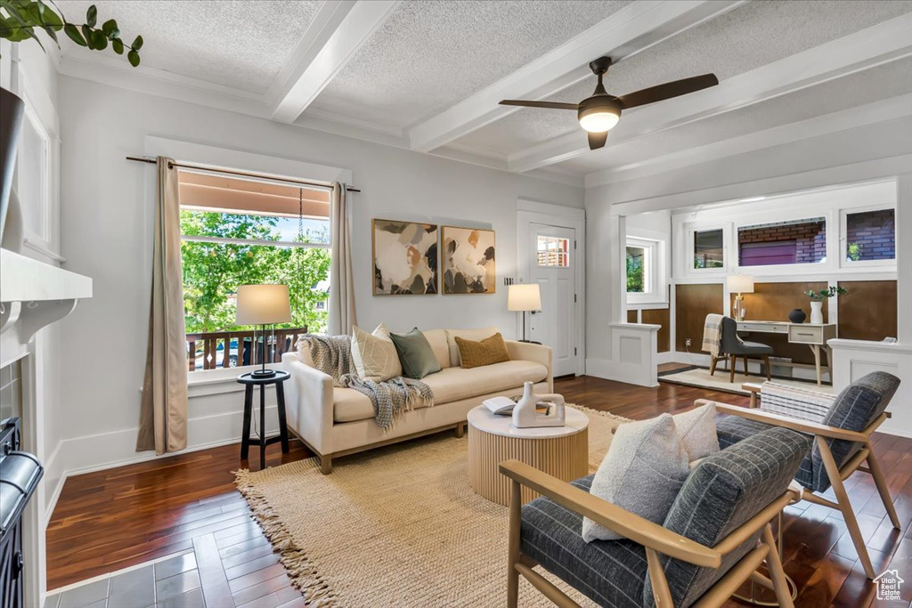 Living area with beamed ceiling, a textured ceiling, hardwood / wood-style floors, a ceiling fan, and a desk