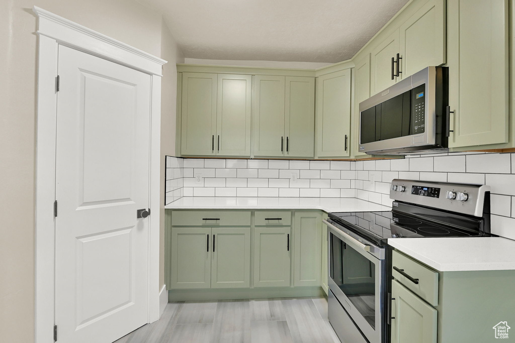 Kitchen featuring green cabinetry, appliances with stainless steel finishes, light countertops, and backsplash