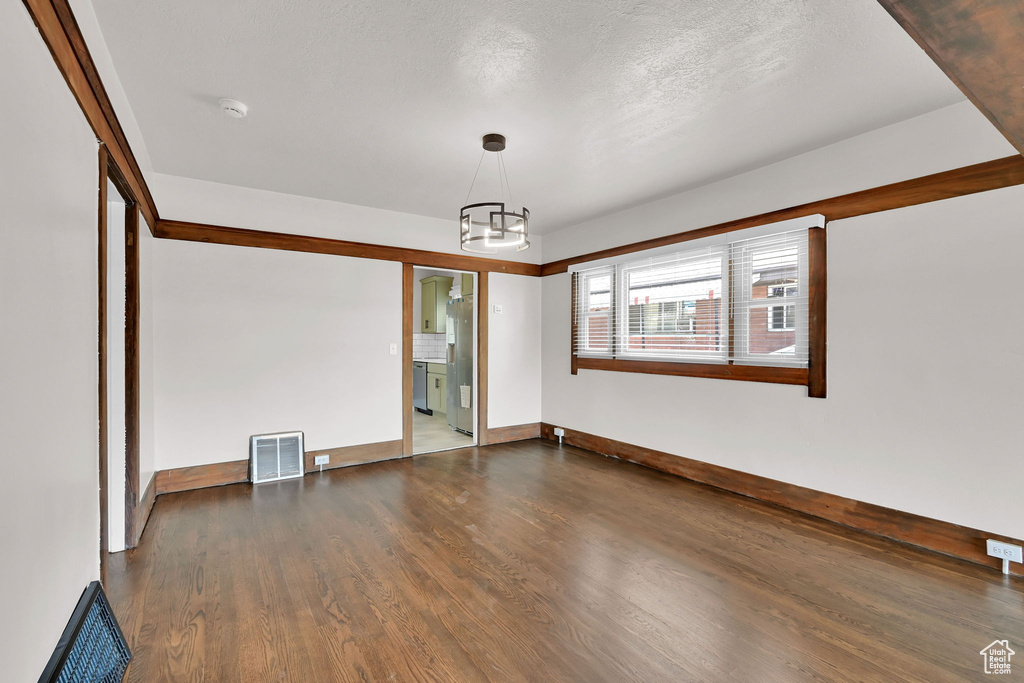 Spare room featuring wood finished floors, a chandelier, and baseboards