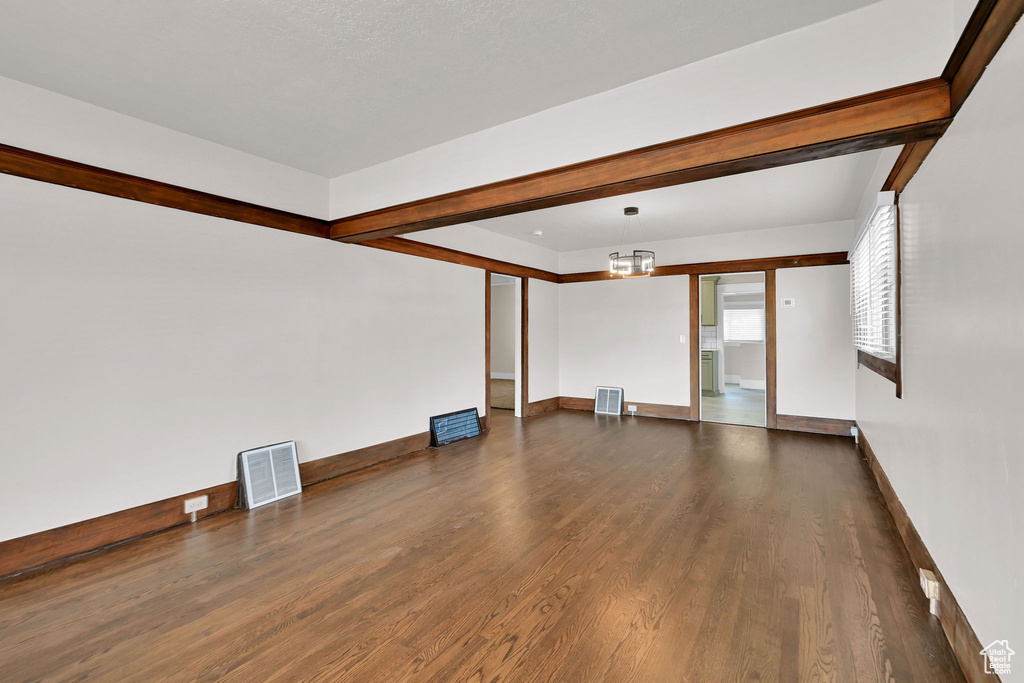 Unfurnished living room featuring dark wood finished floors, baseboards, and a chandelier