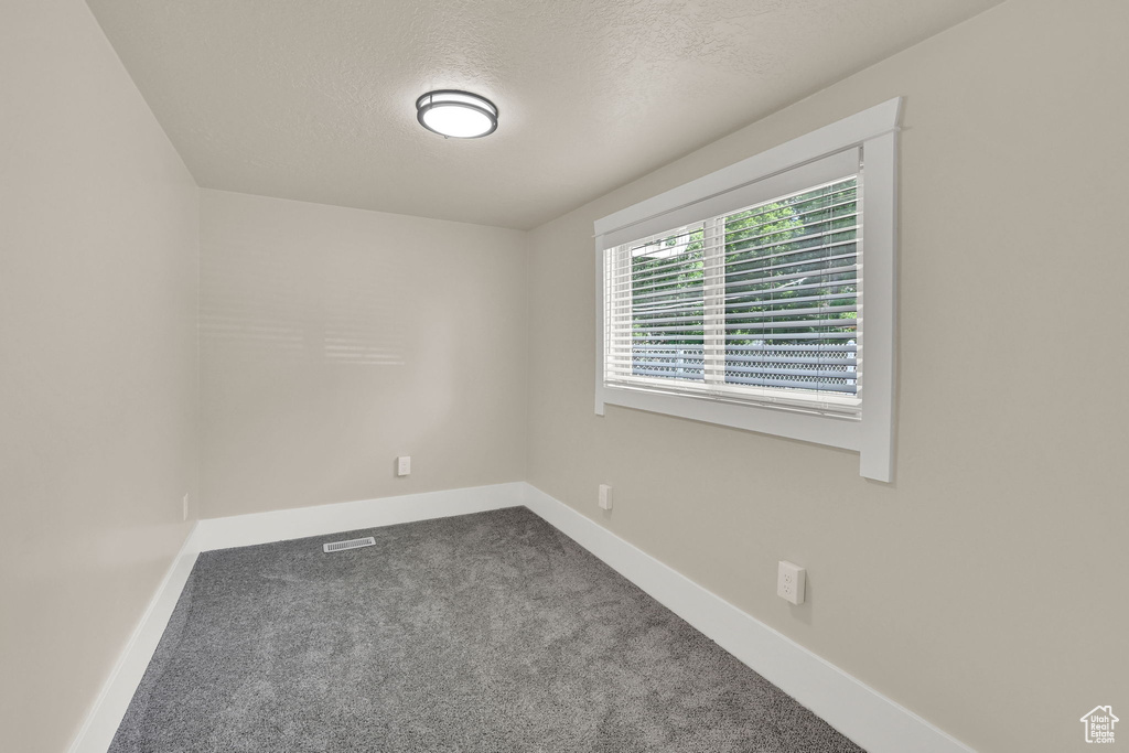 Unfurnished room featuring dark carpet, baseboards, and a textured ceiling