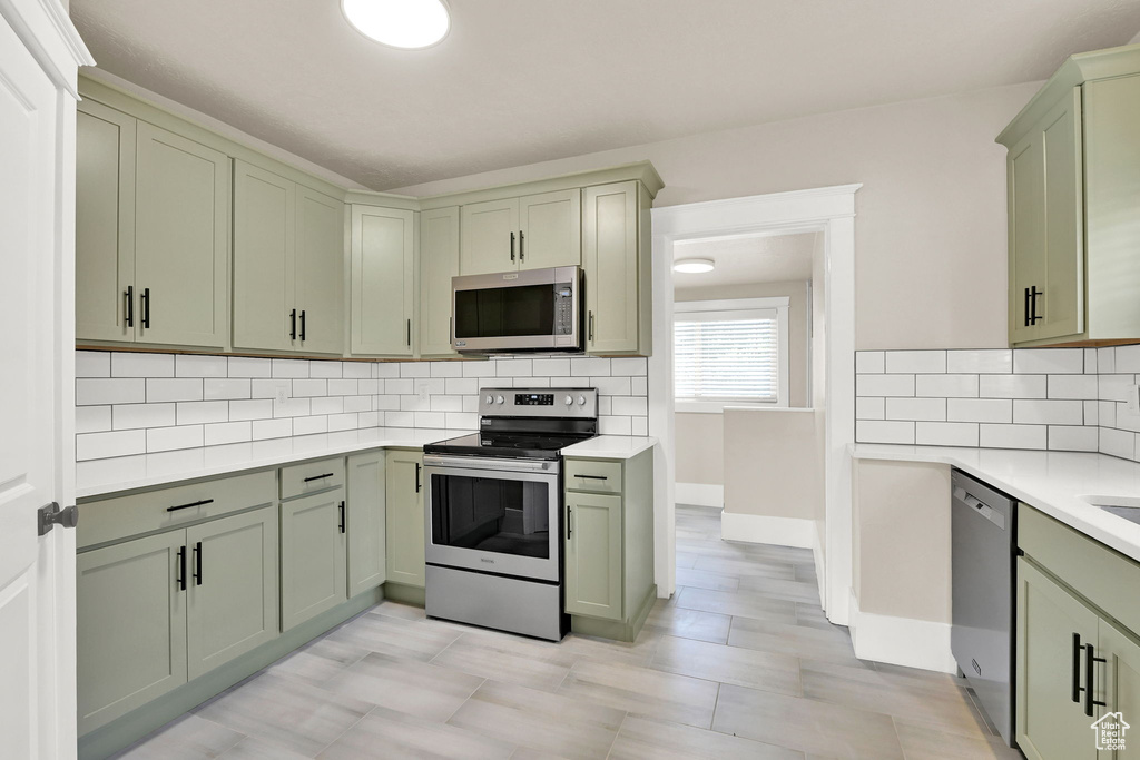 Kitchen with appliances with stainless steel finishes, green cabinets, light countertops, and tasteful backsplash