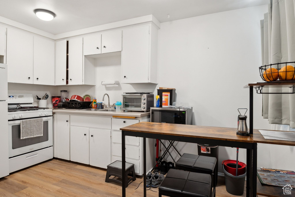 Kitchen with white gas range, a sink, light wood-style floors, and white cabinetry