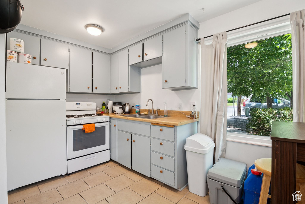 Kitchen featuring white appliances, a sink, light tile patterned floors, and light countertops
