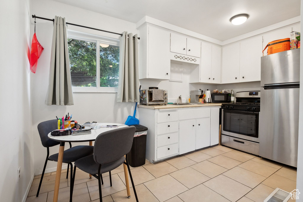 Kitchen featuring stainless steel appliances, white cabinets, light countertops, light tile patterned floors, and a sink