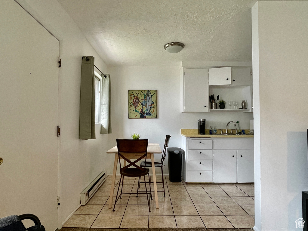 Kitchen featuring a baseboard heating unit, open shelves, white cabinets, light tile patterned floors, and a sink