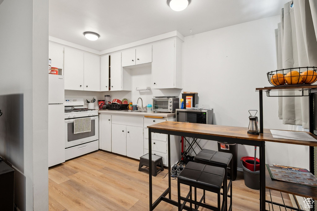 Kitchen with white appliances, light wood-style flooring, a sink, white cabinetry, and light countertops