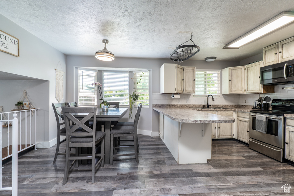 Kitchen featuring stainless steel appliances, a sink, a peninsula, backsplash, and baseboards