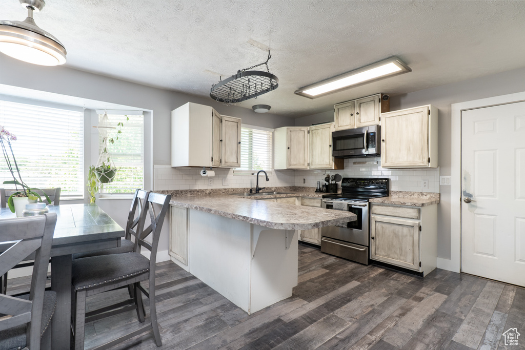 Kitchen with appliances with stainless steel finishes, a peninsula, backsplash, light countertops, and a textured ceiling