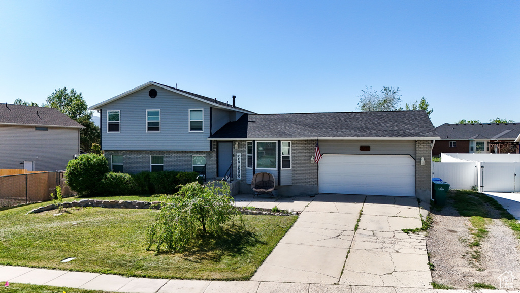 Tri-level home featuring brick siding, an attached garage, driveway, and a gate
