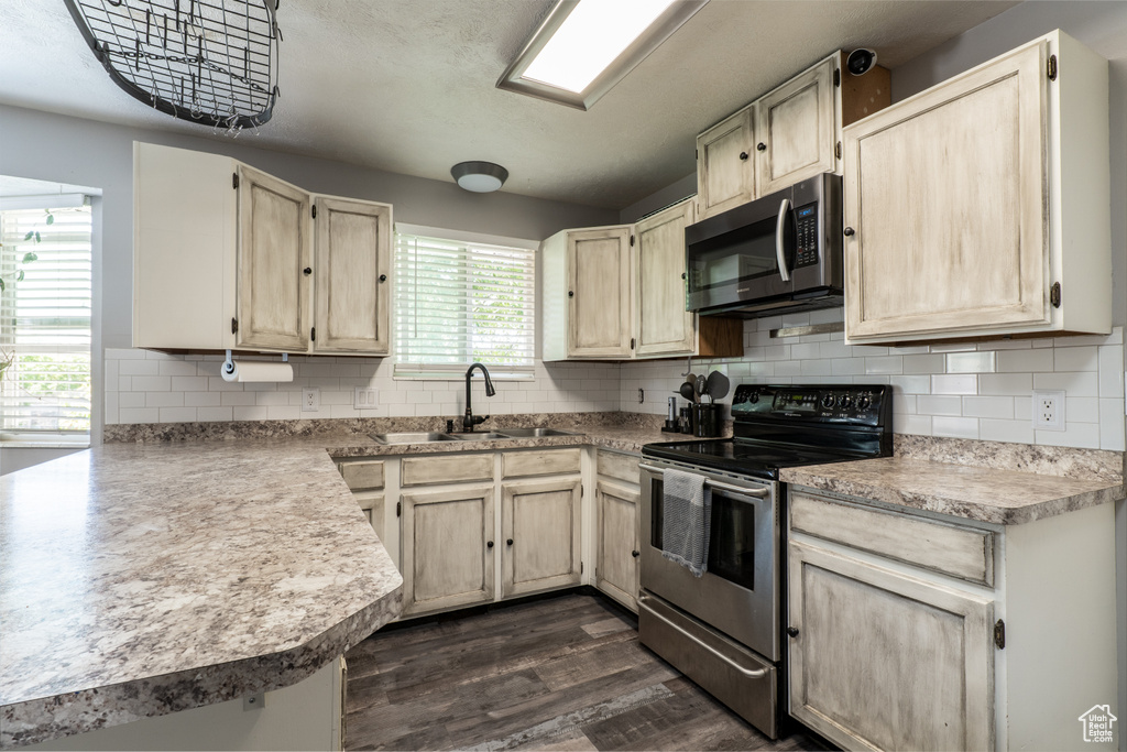 Kitchen featuring appliances with stainless steel finishes, a sink, dark wood-style flooring, backsplash, and light countertops