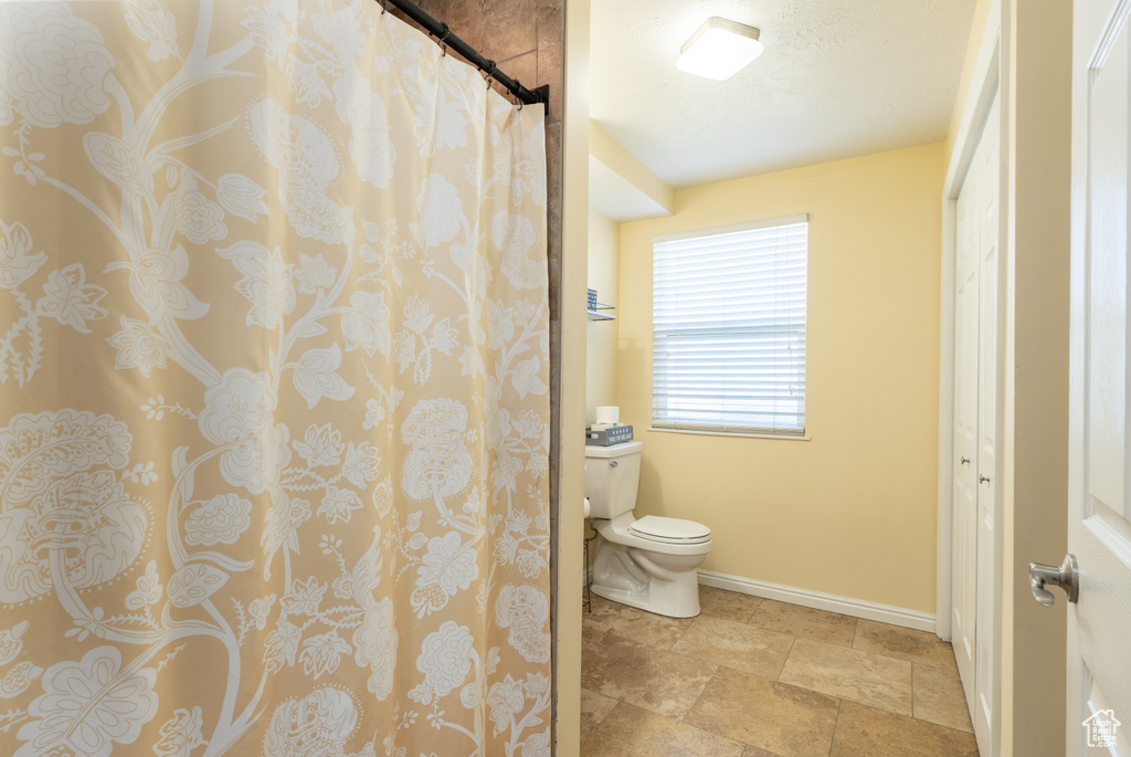 Full bathroom featuring baseboards, toilet, stone tile floors, and curtained shower