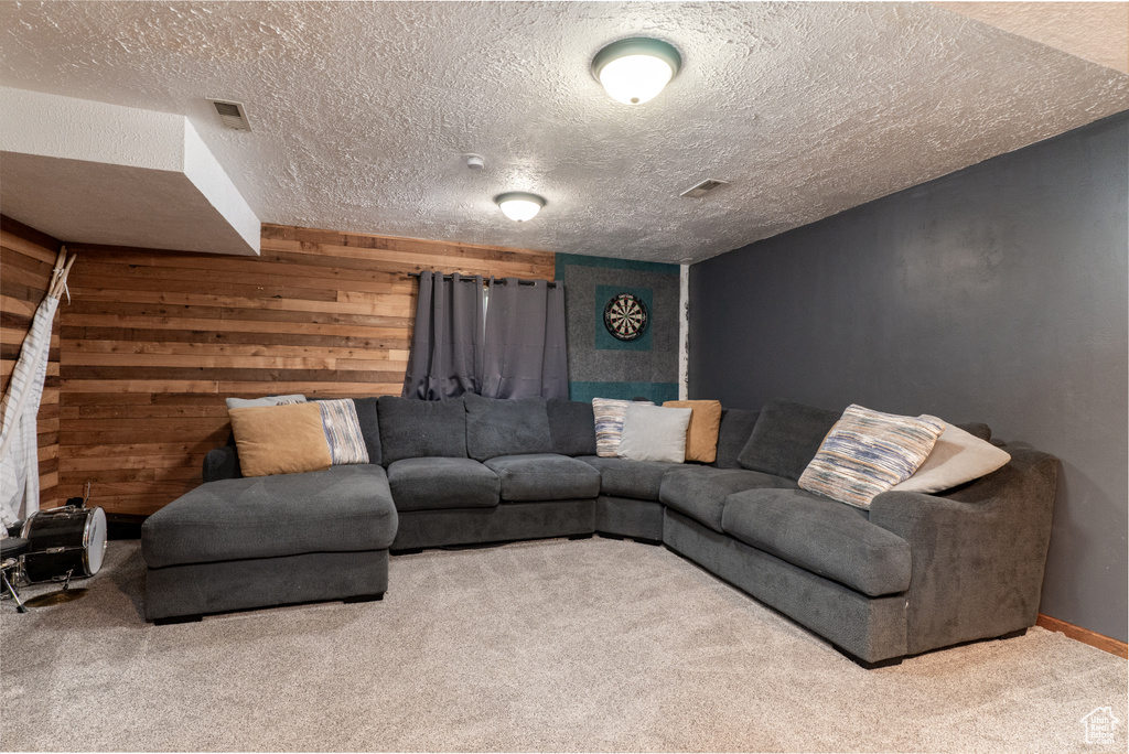 Carpeted living room with wooden walls, a textured ceiling, and baseboards