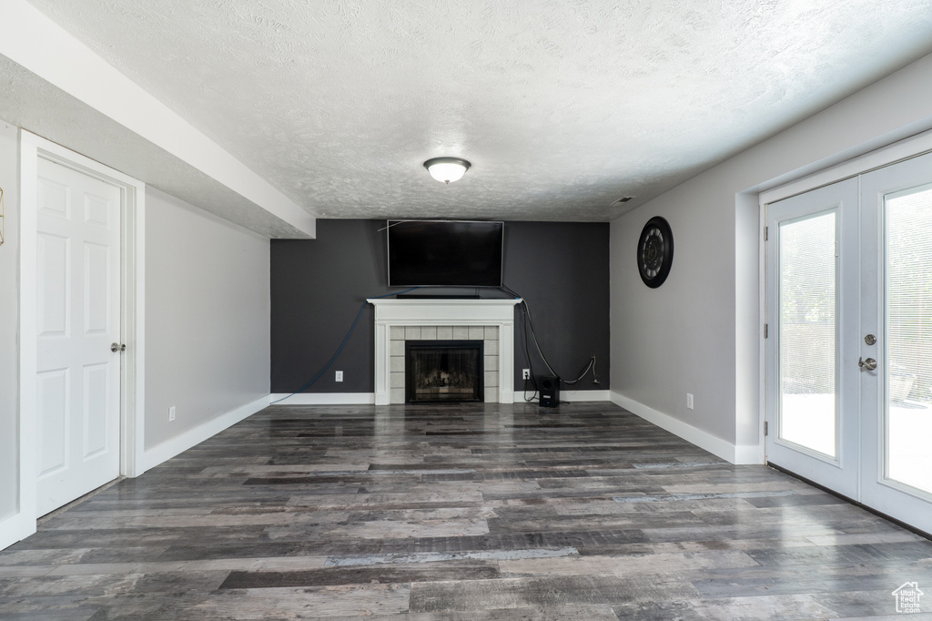 Unfurnished living room with french doors, a textured ceiling, wood finished floors, and healthy amount of natural light