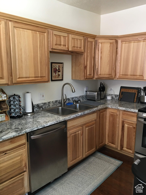 Kitchen with appliances with stainless steel finishes, a sink, and dark wood-type flooring
