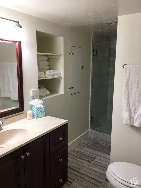 Full bath featuring vanity, a shower stall, toilet, a textured ceiling, and baseboards