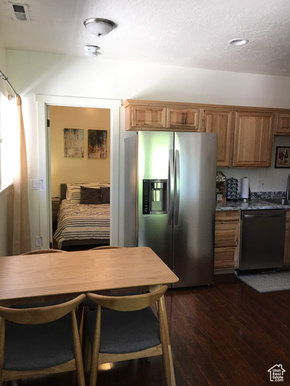 Kitchen with stainless steel fridge, dishwashing machine, dark wood finished floors, brown cabinetry, and a textured ceiling