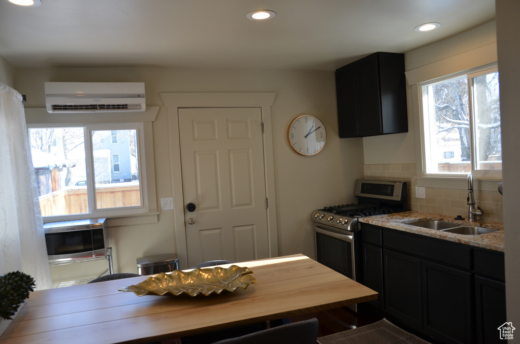 Kitchen with a sink, stainless steel range with gas cooktop, a wall unit AC, dark cabinetry, and recessed lighting