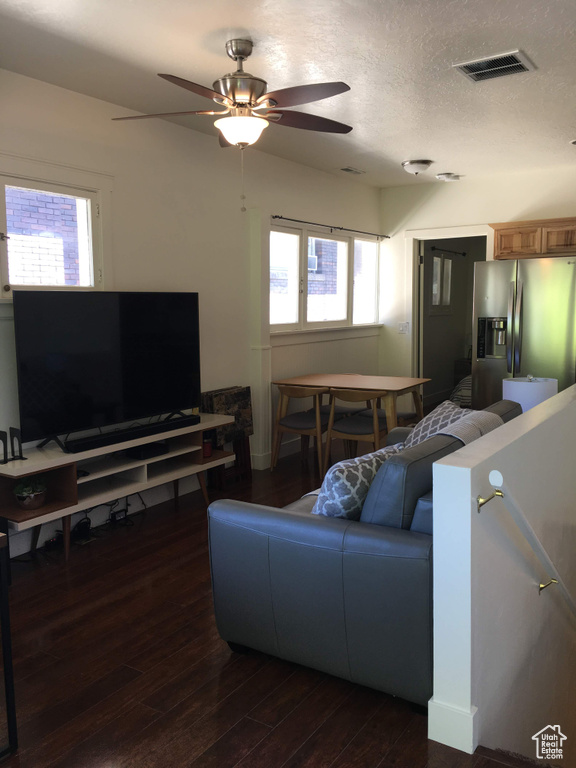 Living area with ceiling fan, dark wood-style floors, and healthy amount of natural light