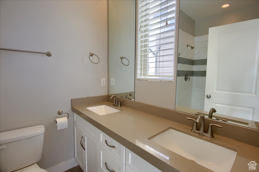 Bathroom with toilet, double vanity, and a tile shower
