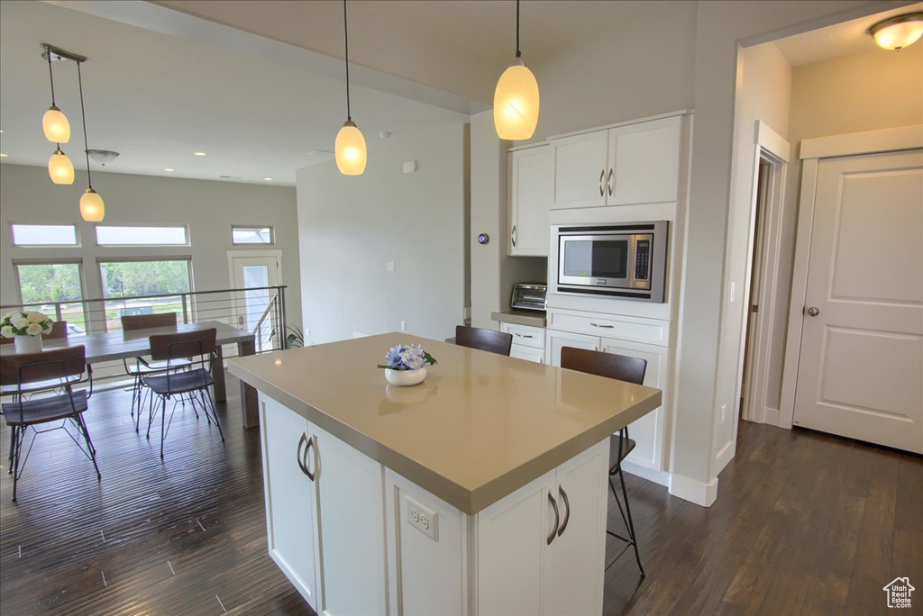 Kitchen with stainless steel microwave, a center island, dark wood finished floors, white cabinetry, and hanging light fixtures