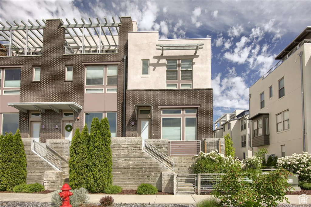 View of front of property featuring stairway, brick siding, stucco siding, and a pergola