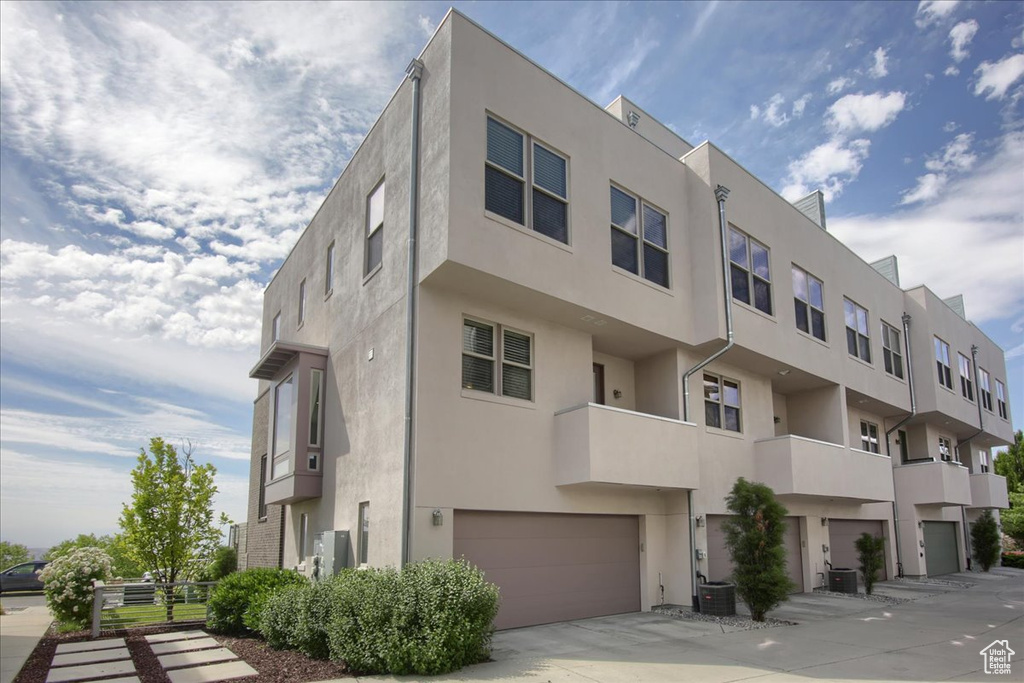 View of building exterior with an attached garage, concrete driveway, and central AC unit