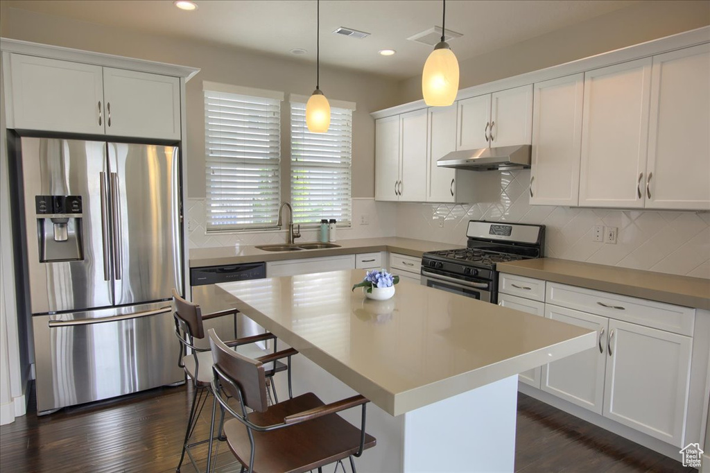 Kitchen featuring stainless steel appliances, under cabinet range hood, a sink, white cabinetry, and tasteful backsplash