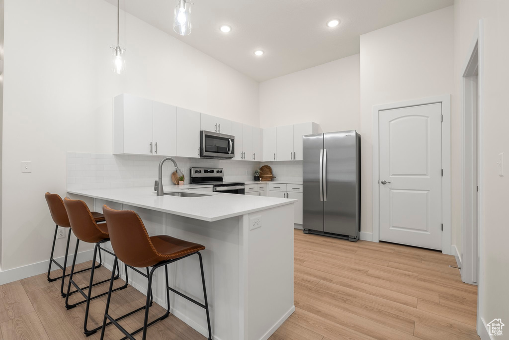 Kitchen with appliances with stainless steel finishes, a sink, a high ceiling, a peninsula, and a breakfast bar area