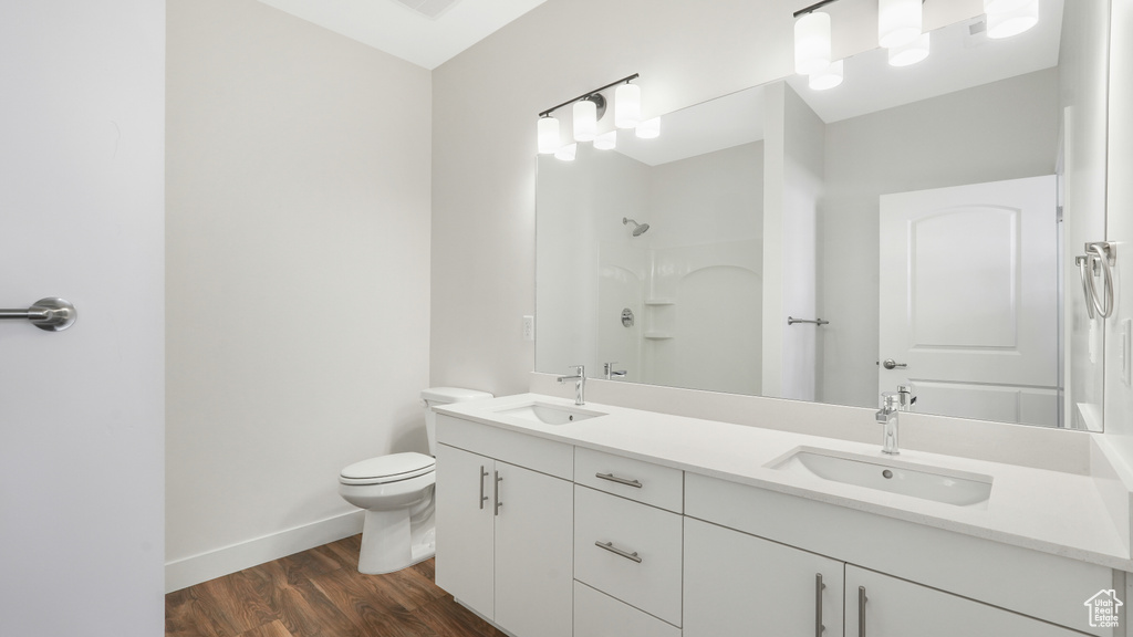 Bathroom with double vanity, toilet, wood finished floors, a shower, and baseboards