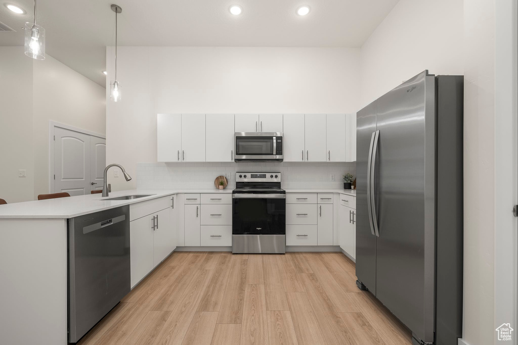 Kitchen featuring appliances with stainless steel finishes, a peninsula, a sink, light countertops, and light wood-style flooring
