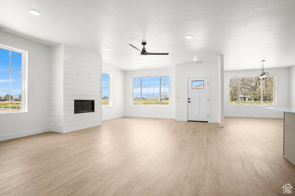 Unfurnished living room with baseboards, light wood-style floors, a large fireplace, a textured ceiling, and recessed lighting