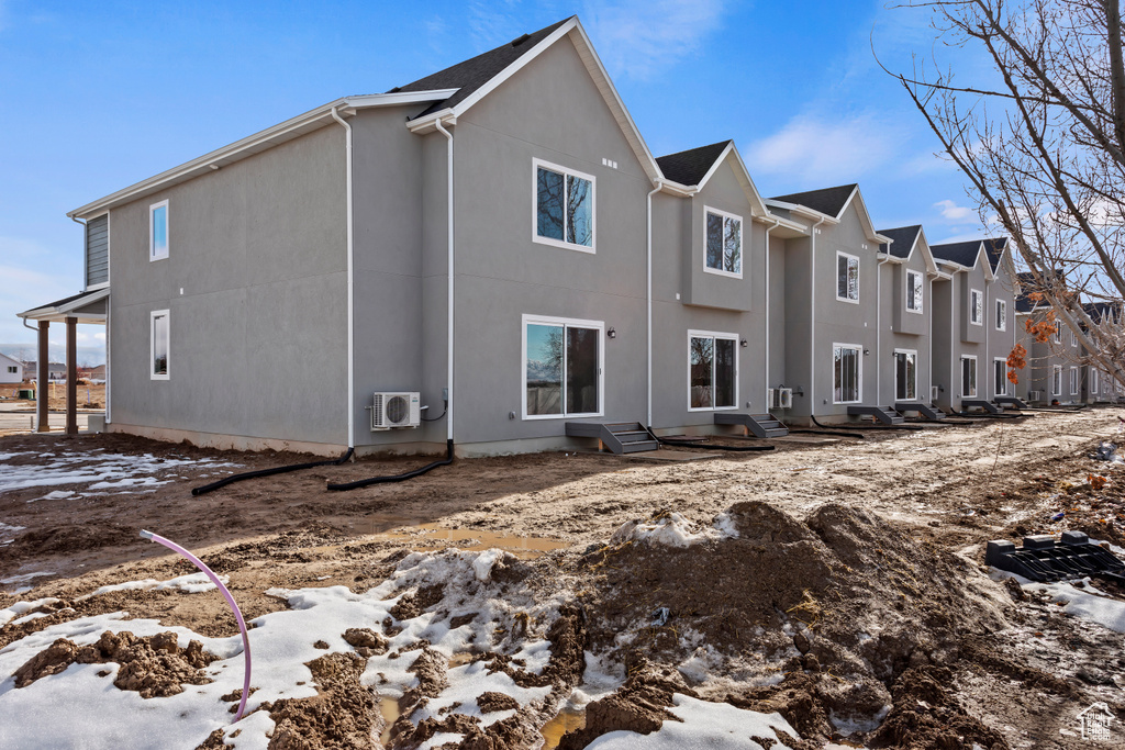 Snow covered rear of property featuring stucco siding, a cooling unit, and entry steps