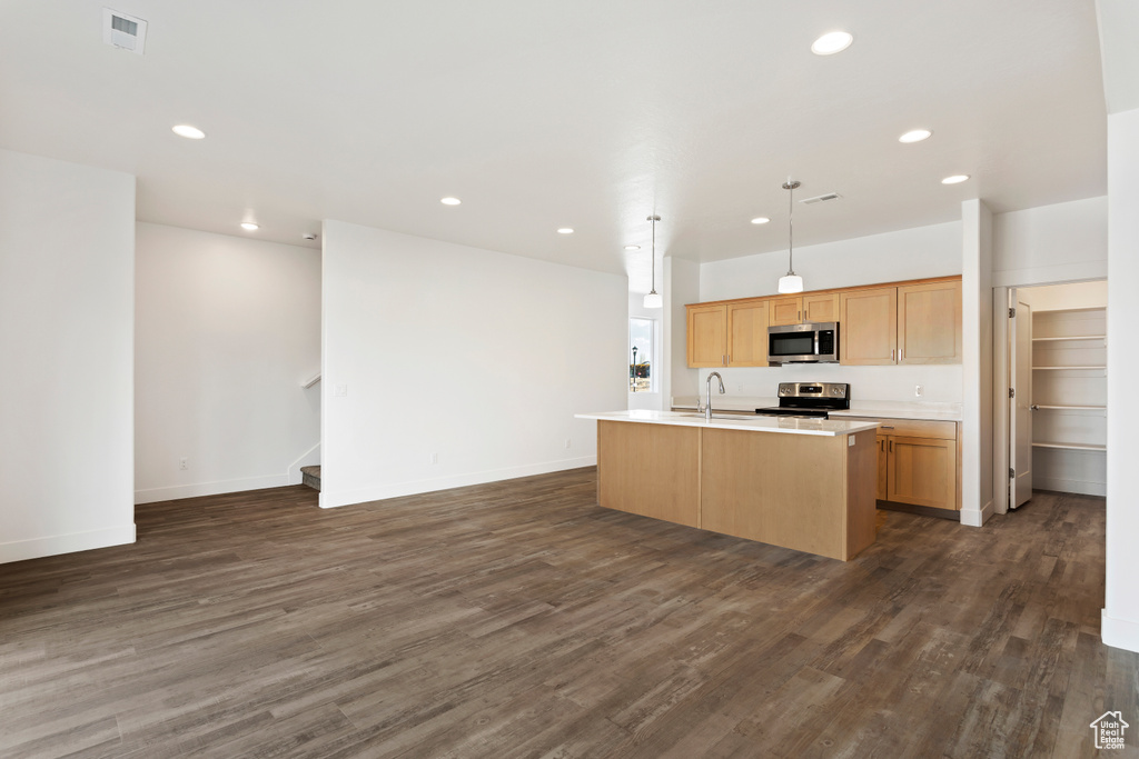 Kitchen featuring stainless steel appliances, dark wood-style flooring, light countertops, a center island with sink, and open floor plan