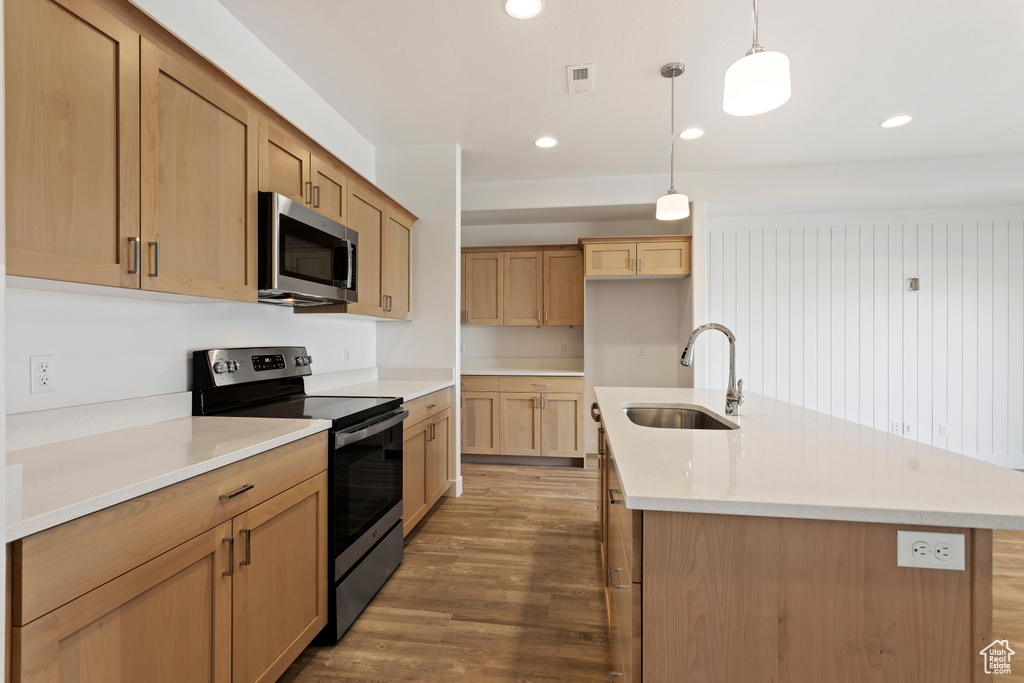 Kitchen featuring stainless steel appliances, a sink, wood finished floors, light countertops, and pendant lighting
