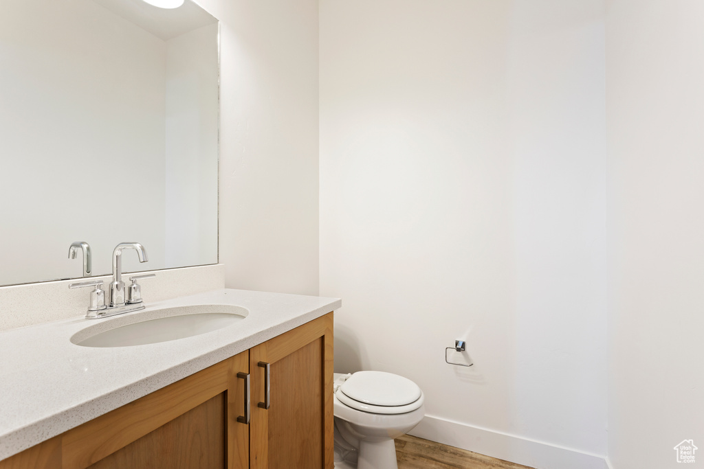 Bathroom featuring vanity, toilet, wood finished floors, and baseboards