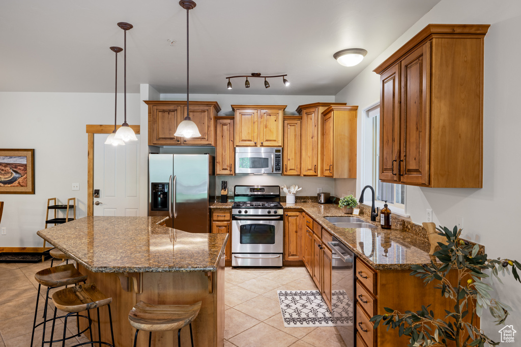 Kitchen with appliances with stainless steel finishes, a sink, light tile patterned floors, brown cabinetry, and a kitchen breakfast bar
