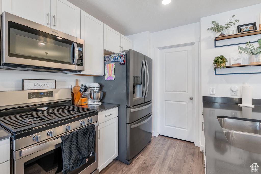 Kitchen with appliances with stainless steel finishes, white cabinetry, light wood-style floors, dark countertops, and a sink