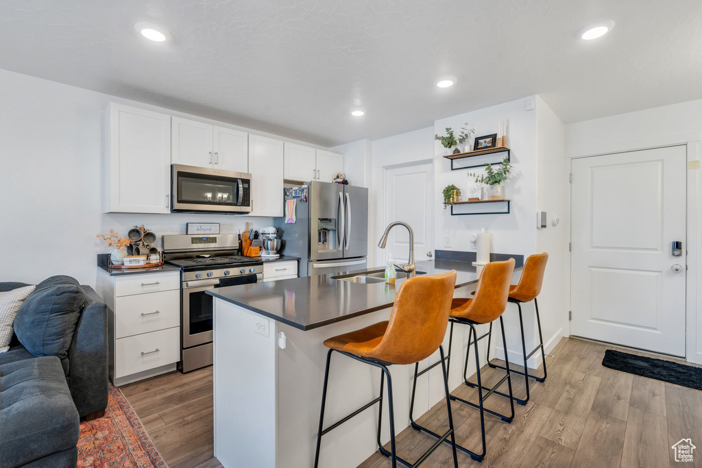 Kitchen with appliances with stainless steel finishes, a sink, dark countertops, a breakfast bar area, and light wood-style floors