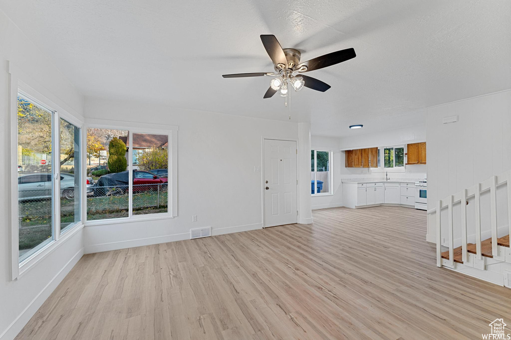 Unfurnished living room featuring light wood finished floors, ceiling fan, baseboards, and a sink