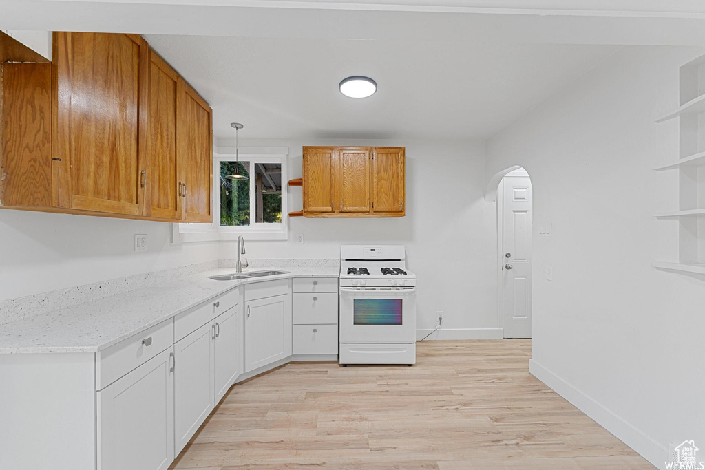 Kitchen with white range with gas stovetop, open shelves, a sink, and arched walkways