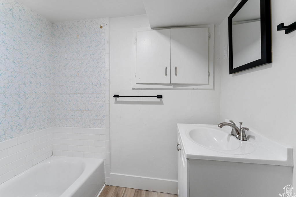 Bathroom featuring vanity, wood finished floors, baseboards, and shower / washtub combination