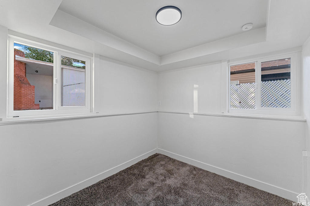 Empty room with a tray ceiling, dark colored carpet, baseboards, and a smoke detector