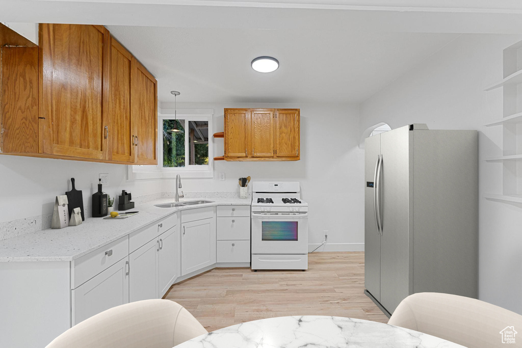 Kitchen with white gas range oven, a sink, refrigerator with ice dispenser, open shelves, and light wood-style floors