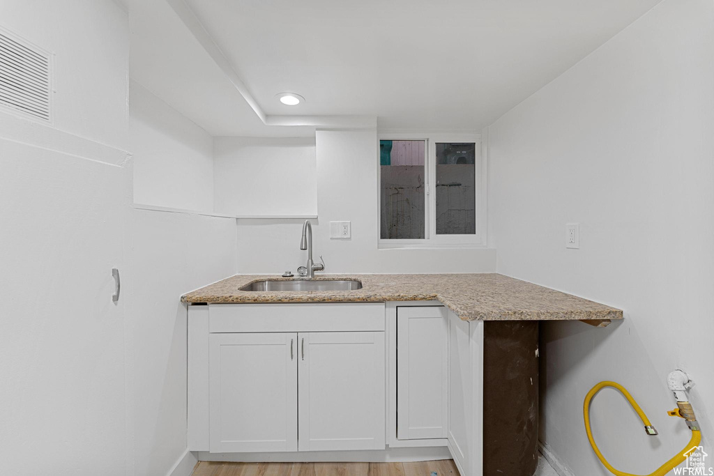 Kitchen with a sink, white cabinetry, baseboards, light wood finished floors, and light stone counters