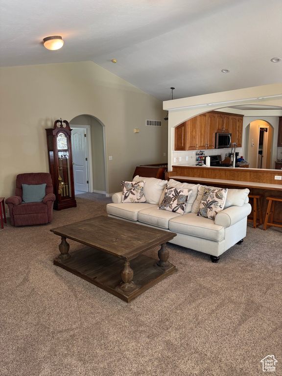 Carpeted living area with arched walkways and lofted ceiling