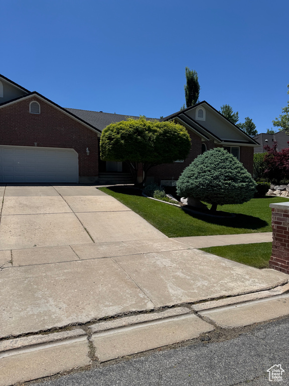 View of front of property with a front yard, driveway, a garage, and brick siding