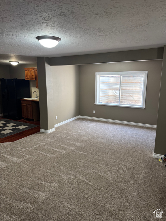 Unfurnished living room featuring a sink, carpet flooring, a textured ceiling, and baseboards